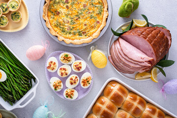 Easter brunch on large table with spiral sliced ham, quiche, deviled eggs and hot cross buns