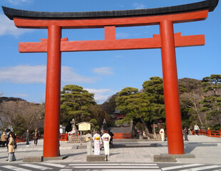 a great red torii gate at the entrance  of a shintoist shrine with three pretty japanese girls...