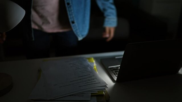 A focused man works overtime on documents and a laptop in a dimly lit office, highlighting dedication and late hours.