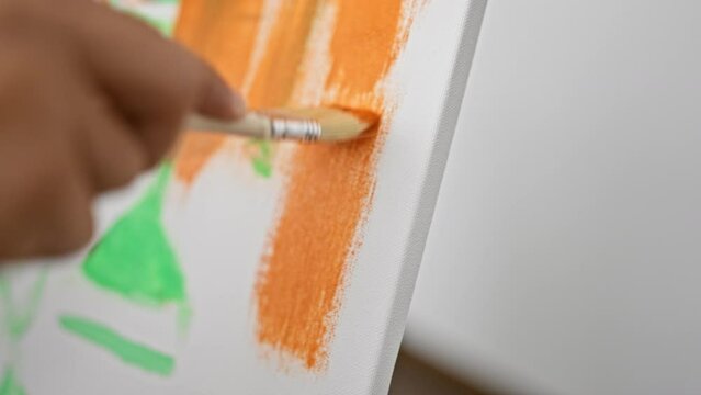 Close-up of a male artist painting an abstract art piece on canvas in a bright studio setting.