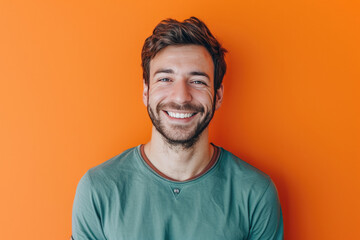 A man with a beard is smiling in front of an orange wall