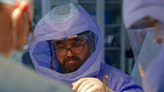 Bearded Caucasian surgeon in glasses and protective helmet. Doctor working in the surgical team.