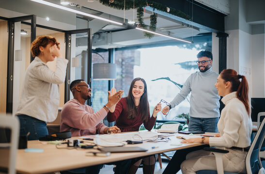 Multicultural coworkers celebrate successful finished project with joy and positive outcomes in the office. Businesswoman and colleagues smiling and caught up in the victory.