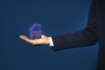 Fototapeta na wymiar Mortgage rate. Man holding virtual house on dark blue background, closeup