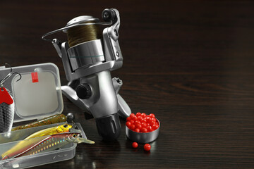 Fishing tackle. Spinning reel, bait and lures on dark wooden background, space for text