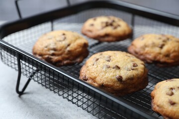Cooling rack with delicious chocolate chip cookies on light grey table, closeup