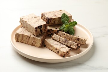 Pieces of tasty chocolate halva and mint on white marble table, closeup