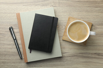 Different notebooks, pen and cup of coffee on wooden table, flat lay