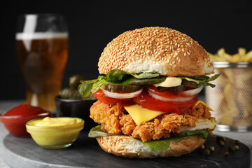Delicious burger with crispy chicken patty and sauces on grey table, closeup