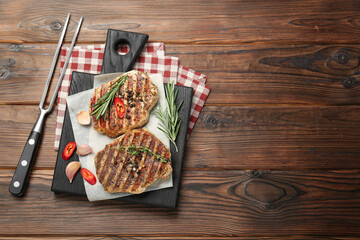 Delicious grilled pork steaks with spices and meat fork on wooden table, top view. Space for text