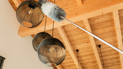 Ceiling lights cleaning.fluffy bristle brush cleans lamps under a wooden ceiling. Fluffy duster and...