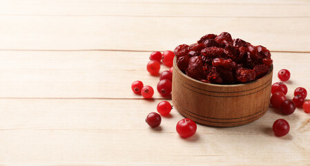 Dried cranberries in bowl and fresh berries on wooden table, space for text