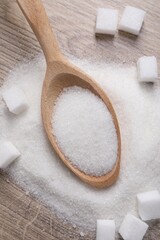 Different types of white sugar and spoon on wooden table, top view