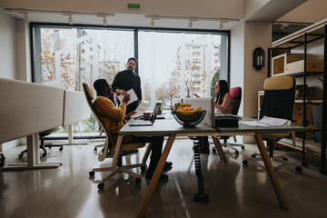 A multicultural team collaborates in a bright office setting, with one man standing and leading the...