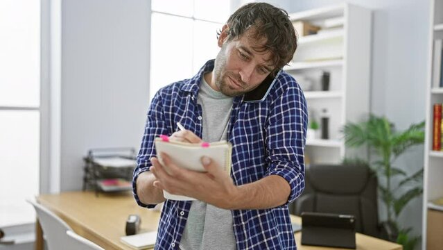 Young, hard-working man busily taking notes and speaking on his office phone