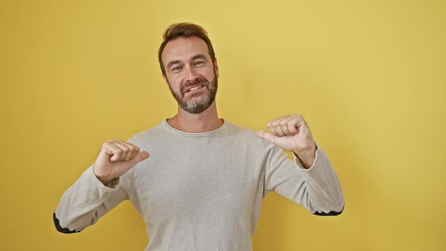 Young hispanic man standing looking confident with smile on face, pointing oneself with fingers proud and happy. over isolated yellow background