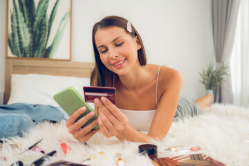 Young woman lying on the bed using online payment app and digital wallet on smartphone to pay with...