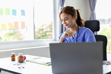 Attractive Asian female doctor doing paperwork with laptop writing prescription in hospital office.