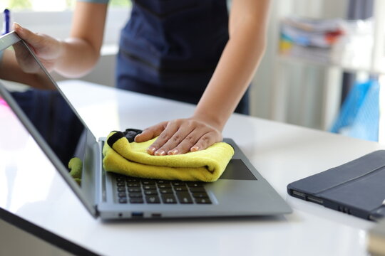 Young Asian cleaning woman uses a towel to clean a computer using cleaning solution in her home office.
