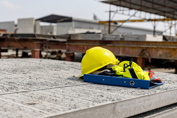 A set of helmet and safety vest left on prefab floor in a factory ready to be used by foremen or constructors.
