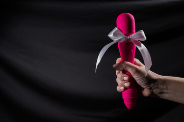 Woman holding pink vibrator with white bow on black background. Copy space. 