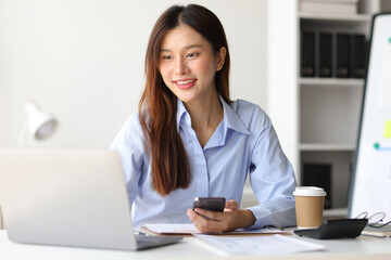 Asian woman in office is using mobile phone and calling someone, she is smiling with joy and surprise when receiving good news.