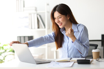 Asian woman in office is excited and happy while looking at surprise laptop screen.