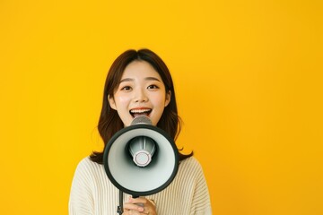 Smiling Asian woman with loudspeaker, making announcement, vibrant yellow background