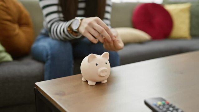 Young woman saving money in a piggy bank in cozy home interior with a sofa in the background.