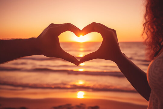 A couple are holding their hands together in a heart shape at the beach. romantic sunset at the beach