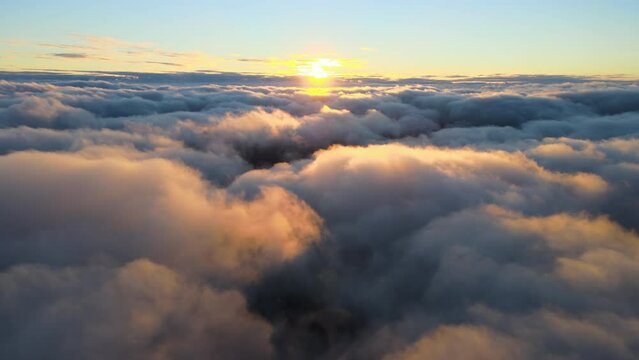 Aerial view from above at high altitude of dense puffy cumulus clouds flying in evening. Amazing sunset from airplane window point of view.