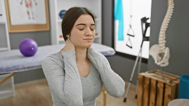 A young hispanic woman experiencing neck pain at a clinic, highlighting healthcare and therapy indoors.