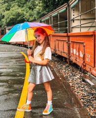 Little girl smiling holding a rainbow umbrella in her arms with vintage train on the background....