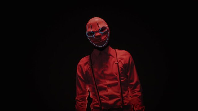 Male pantomime artist with scary mask on his face doing slow creepy moves against black background