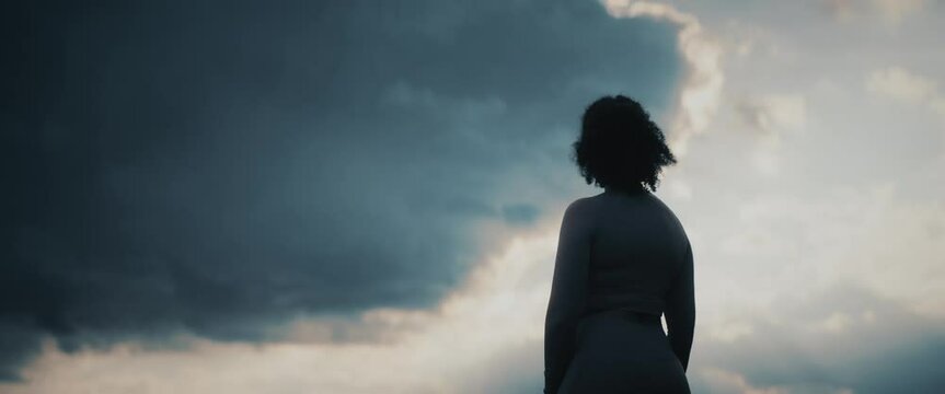 Panoramic back shot of a young woman in sportswear standing against cloudy dawn sky