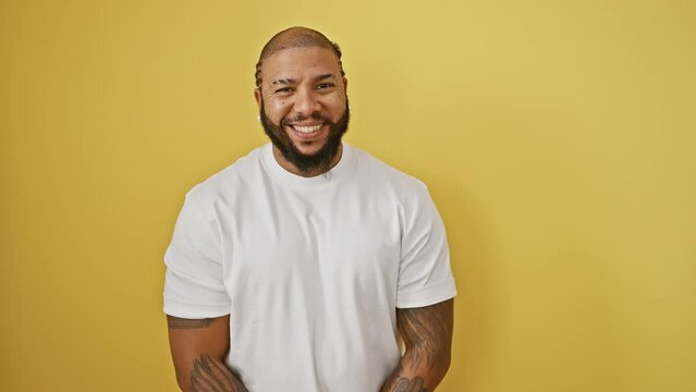 Lucky african american man, smiling in pure joy, proudly standing in front of a yellow isolated background, a model of success, positive lifestyle, and cool confidence.