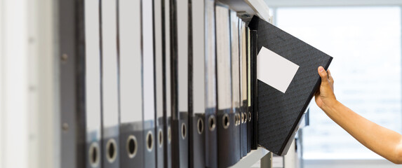 Hand of businessman office worker searching files and paperwork in the archive or document archiving storage room shelf for folder binder finding or data report record or workplace photo concept. - obrazy, fototapety, plakaty