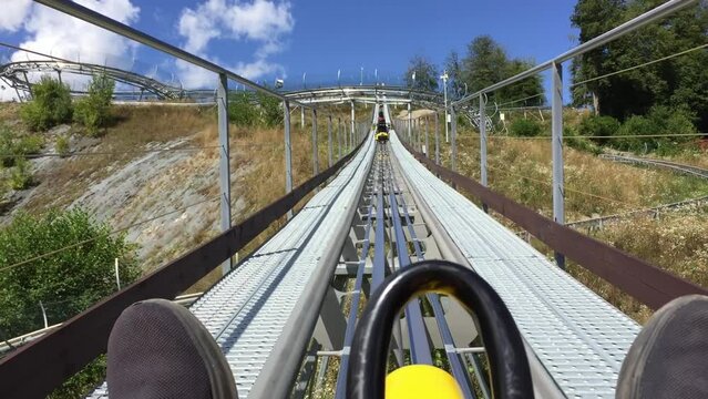 POV person riding coaster on nature in mountains in amusement park. Outdoor recreation, entertainment, enjoy extreme downhill. Adventure in mountain enjoying having fun on roller coaster in sunny day.