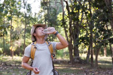 Asian male traveler carrying a large backpack drinks from a bottle while resting during a hiking trip.