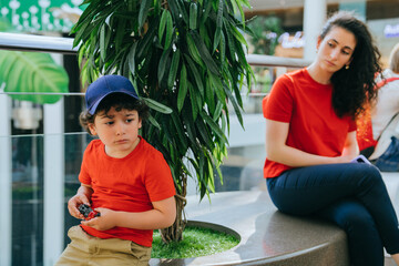 Young boy in a cap sitting by a woman in a mall, family time and modern lifestyle