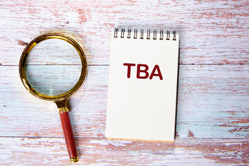 TBA (abbreviation of to be announced) a word written on a notebook on wooden boards next to a...