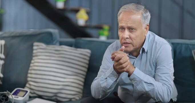 Asian India retired old elder tired senior man sitting alone sofa couch feel bad sorrow indoor home Indian middle aged older adult tense lost male think lonely suffer ill sick health living room house
