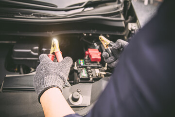 Close-up hand auto mechanic using connect jumper cables on terminal dead battery for jump-start or...