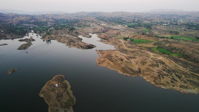 aerial drone shot flying forward over alsigarh lake with small island with white house surrounded by Aravalli hills in city of udaipur in rajasthan a popular tourist spot