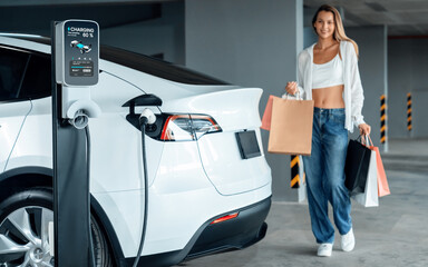 Young woman travel with EV electric car to shopping center parking lot charging in downtown city...