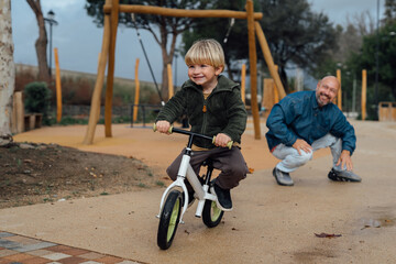 Dad teaches his son riding on bicycle in park. Father and son smile and have fun together