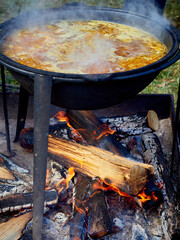 Camping food is cooked over a fire in a cauldron