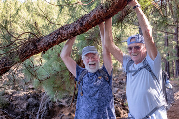 Cheerful couple of old active men with hat and backpack embrace have fun in mountain hike in the...