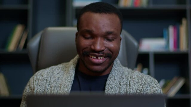 Refocus from the laptop to the face of a black man working online, a black psychologist at a laptop working online, a black man counseling online at a laptop, smile, win, be liked.