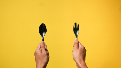 Man's hand holding a black spoon and fork on a yellow background